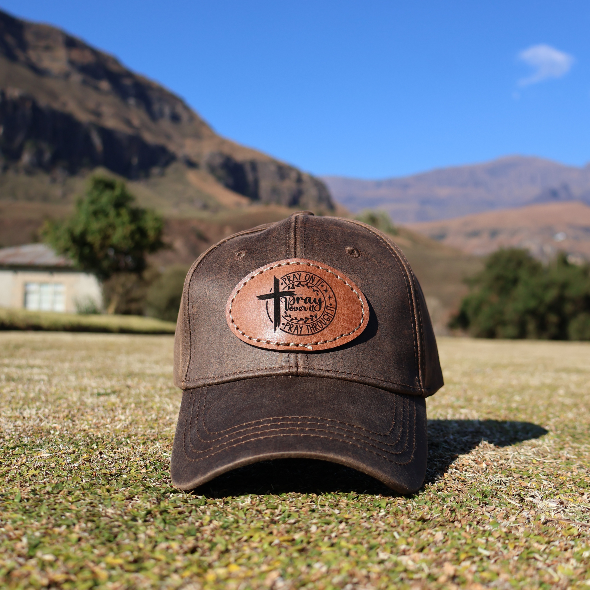 Brown cap with leather patch on grassy field with mountains in the background