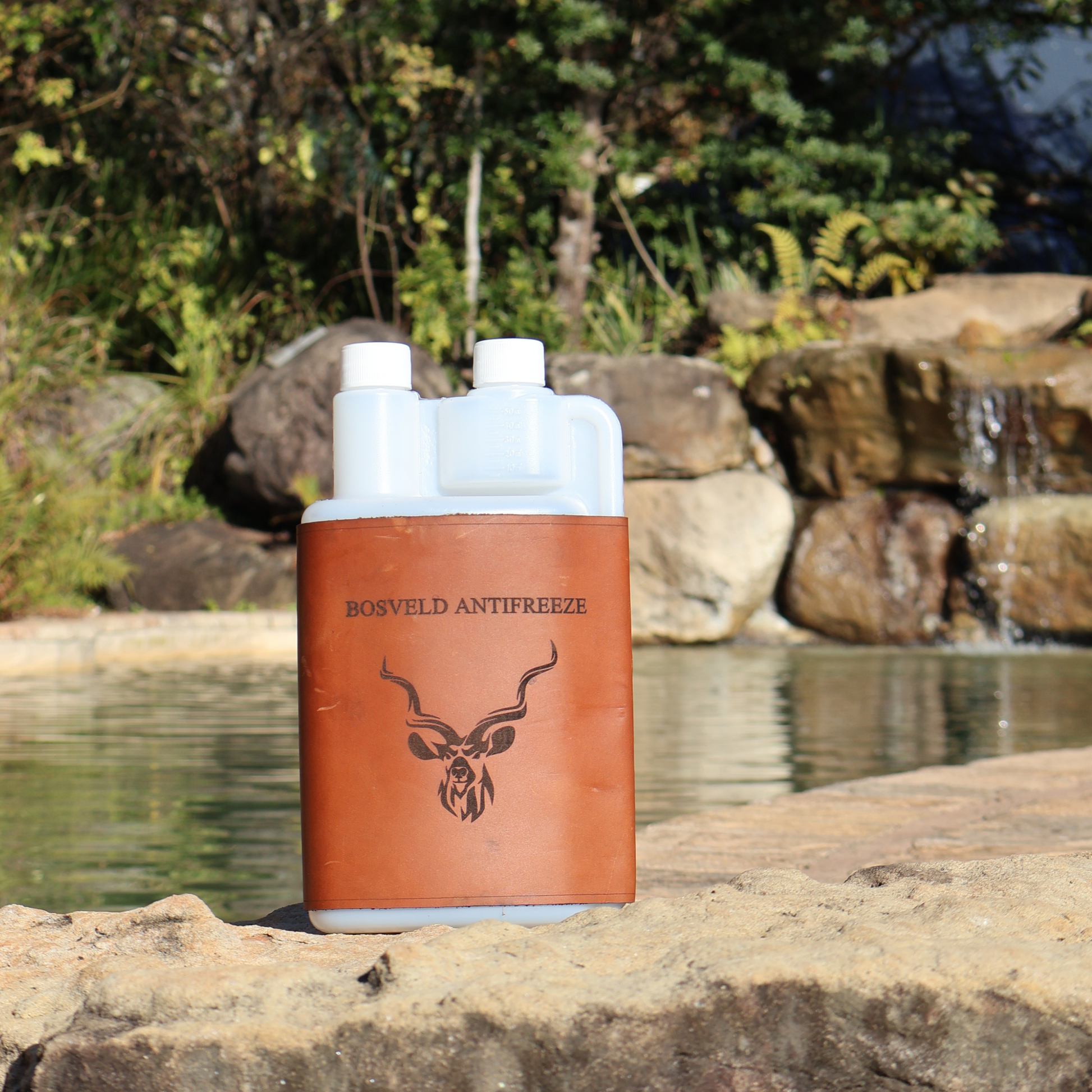 Bosveld Antifreeze plastic squeezy bottle with leather sleeve on a rock by a water body