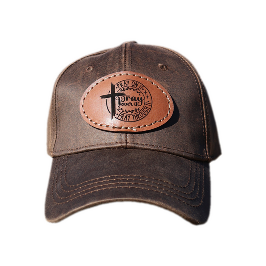 Brown oilskin cap with genuine leather patch engraved with prayer text and cross, on white background