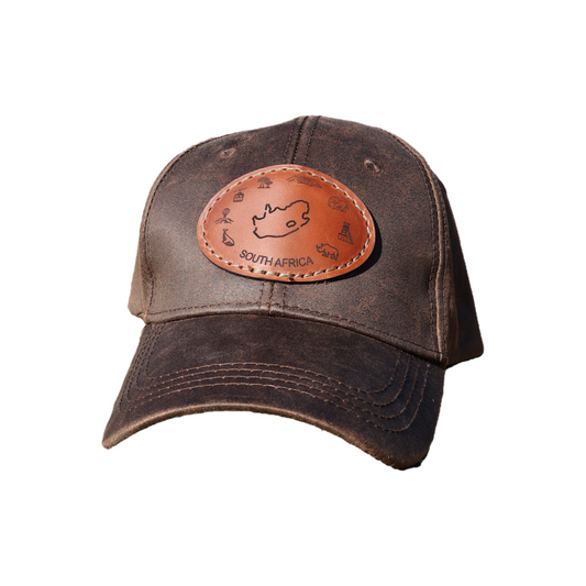 Brown oilskin cap with engraved leather patch featuring South Africa outline and iconic landmarks, on a white background