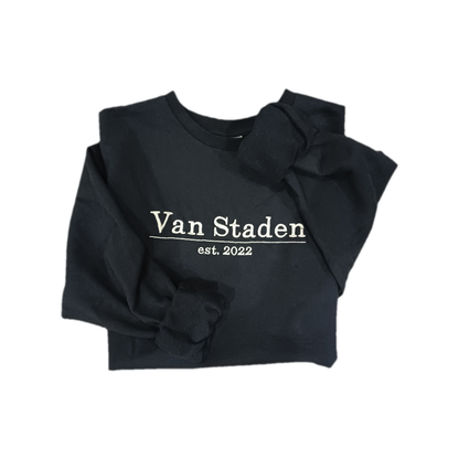 Folded navy sweatshirt with rolled sleeves showing soft inner fleece and personalised white embroidered surname and established date on the front