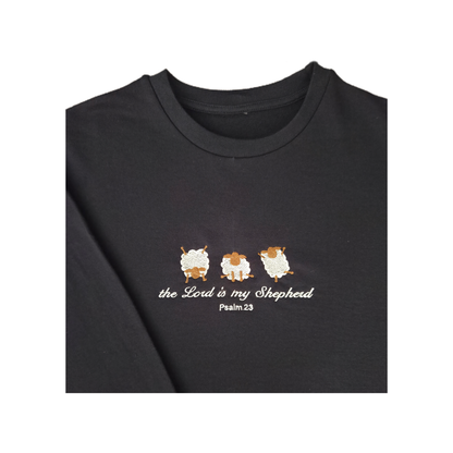 Close-up macro shot of the detailed satin stitch embroidery on a navy sweatshirt, showing three cute textured sheep and white script lettering for the Christian bible verse Psalm 23.