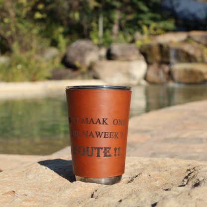 400ml stainless steel glass with leather sleeve engraved “Wat Maak Ons Hierdie Naweek? Foute!!” resting on a rock near a natural pool and waterfall.